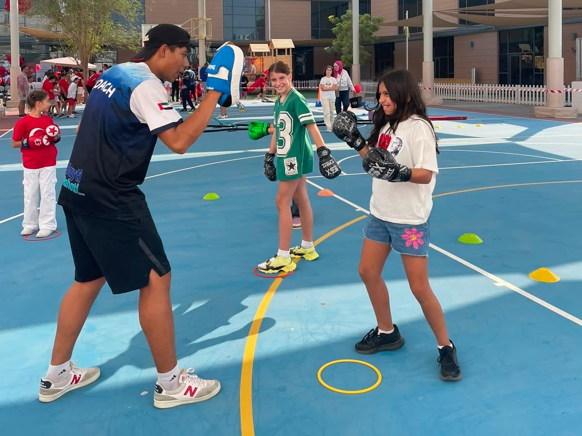 A Wolf Kids coach holding pads for young boxers during an outdoor boxing session