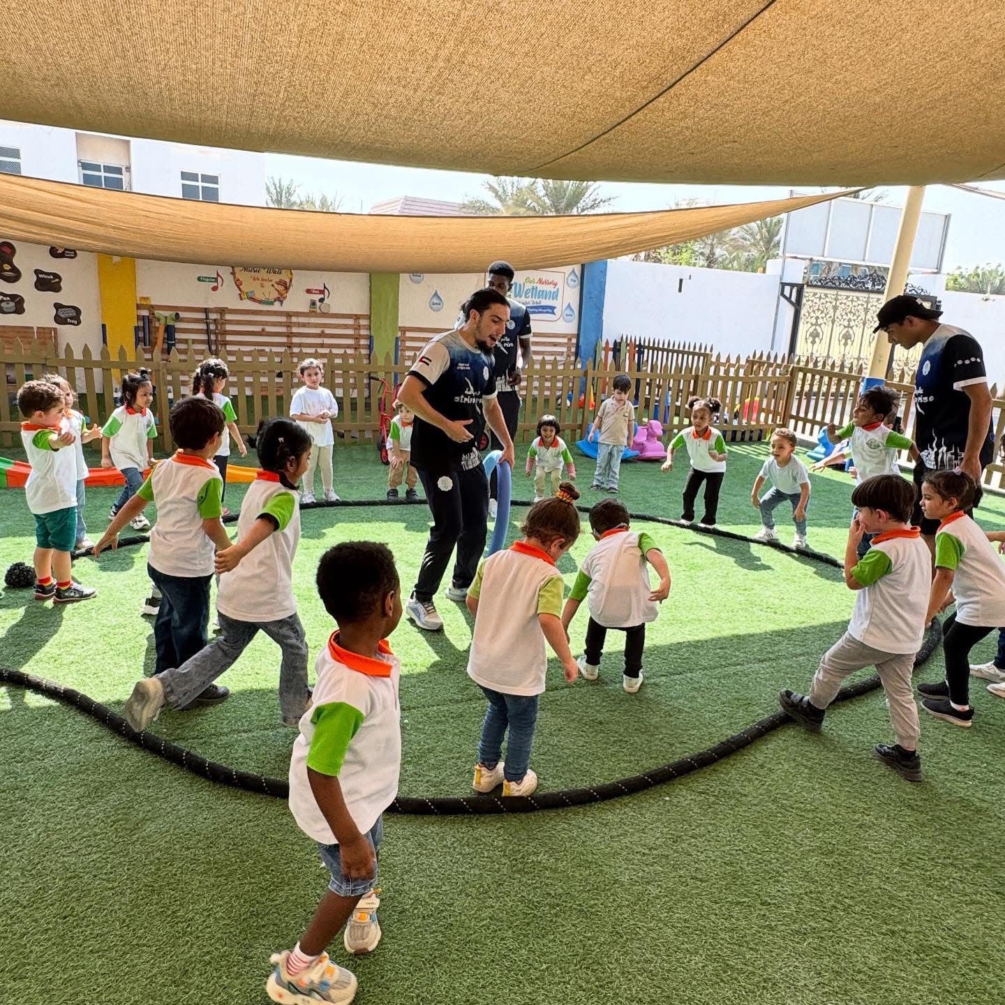 Young children and coaches playing with hoops and soft equipment outdoors.